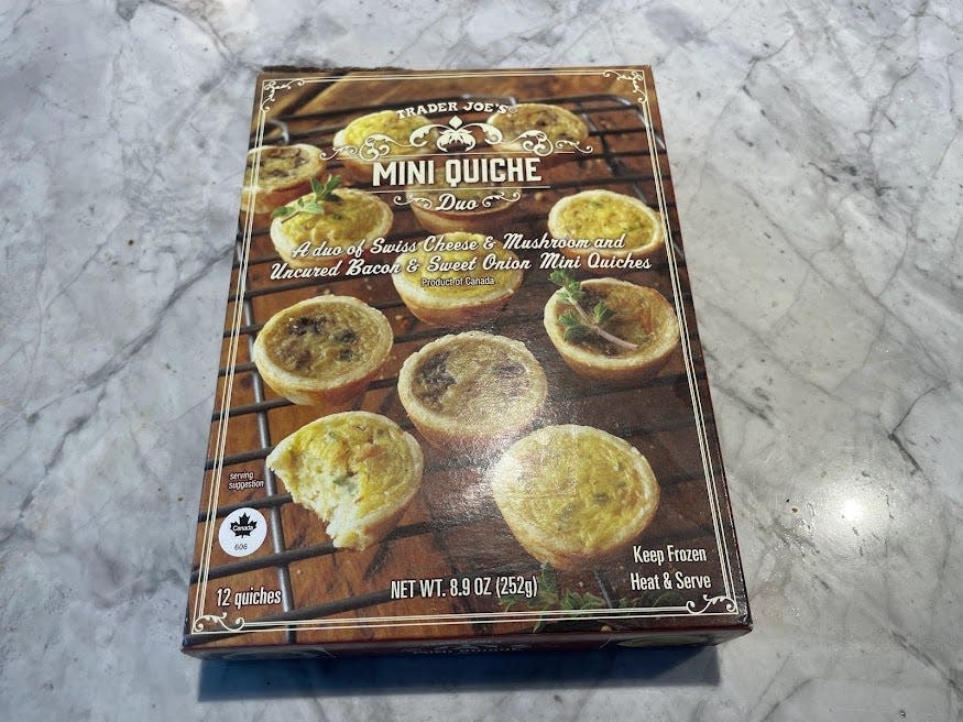 Brown box of Trader Joe's mini quiche duo with photo of quiches on the packaging on a gray counter