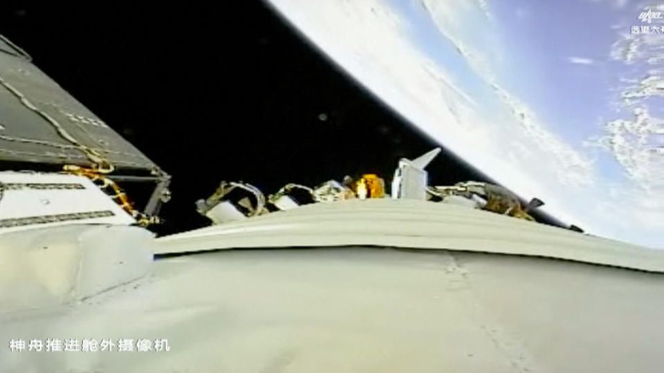 a white spacecraft in the foreground, with the curvature of earth and the blackness of space in the background.