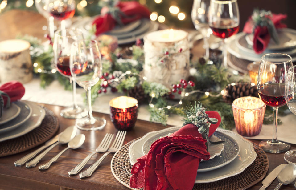 Christmas holiday dining table elegant place setting with red serviettes and candles and red wine and holly. Very shallow depth