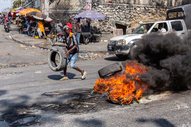 <p>Guerinault Louis/Anadolu via Getty </p> A man sets a tire on fire during a demonstration against CARICOM for the decision following the resignation of Haitian Prime Minister Ariel Henry as representatives of the Caribbean Community (CARICOM) and Haitian actors made an agreement for political transition in Haiti it a historic decision that was made by the formation of a seven-member Presidential Council (CP), and the Haitian government on Tuesday extended the night-time curfew and state of emergency in the capital of Port-au-Prince for a month amid a wave of violence triggered by armed groups in Port-au-Prince, Haiti, on March 12, 2024.