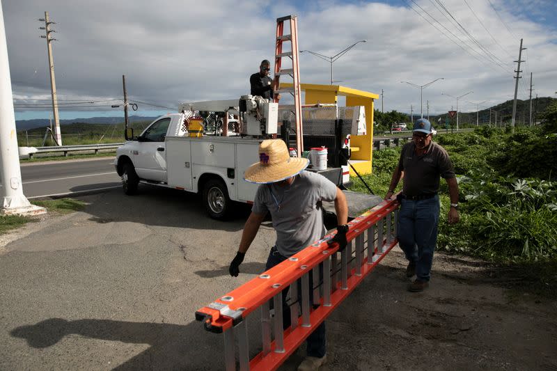 Men carry a ladder as they work fixing power lines after an earthquake in Guanica