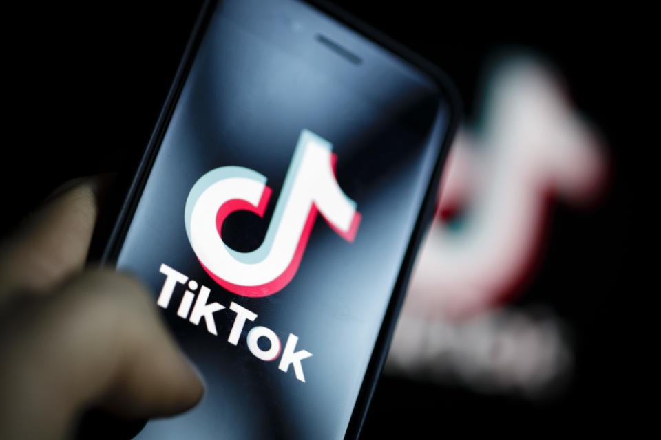 A close-up picture of a hand holding a phone with the TikTok emblem. 