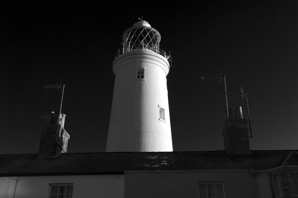 Black and white urban street with lighthouse appearing over roofs at sunrise