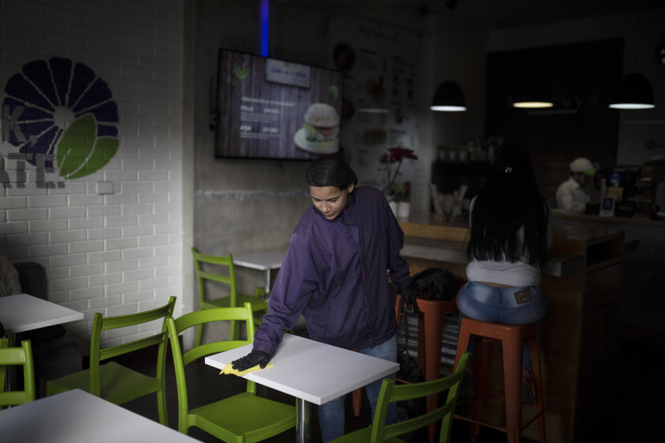 In this Dec. 11, 2018 photo, Venezuelan migrant Emili Espinoza wipes a table clean at the health food restaurant where she works in Bogota, Colombia. Espinoza said that since returning to work in Colombia, she's earned enough money to at least ensure that her children, who are in Venezuela, are able to eat every day. (AP Photo/Ivan Valencia)