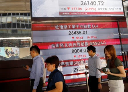 People walk past a screen showing stock indexes in Hong Kong