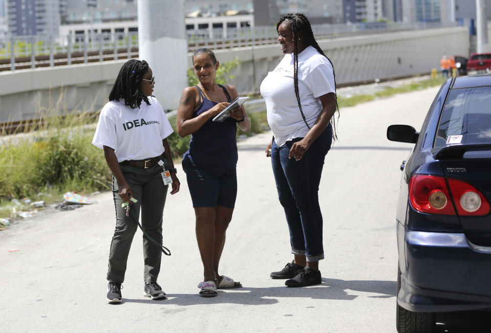 In this Wednesday, July 24, 2019, photo Ivette Naida, center, talks with social worker Elisha Ekowo, left, and Chevel Collington, right, both of the IDEA Exchange, in Miami. Naida is participating in the University of Miami-sponsored program, which provides HIV-infected homeless people with secure medication lockers or delivers small quantities of medicine to them directly. Naida, who was diagnosed with HIV more than a decade ago, lives underneath a Miami highway overpass and has no safe place to keep her belongings. (AP Photo/Lynne Sladky)