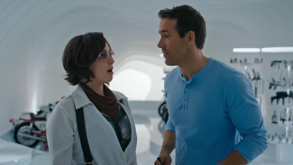 A woman and a man stand close to each other in a large white room