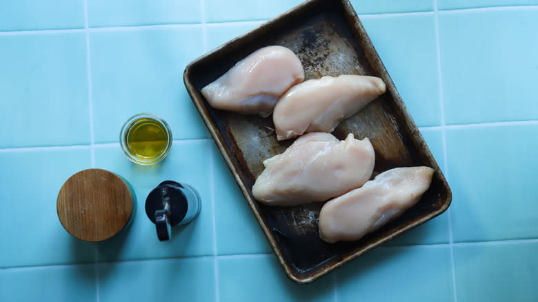 Raw chicken breasts on tray next to oil and sesaonings