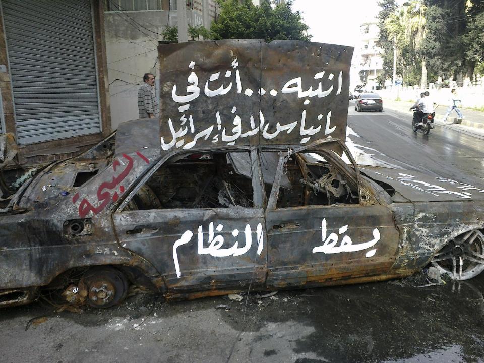 FILE - In this April 17, 2011, file photo, a citizen journalism image made on a mobile phone and acquired by the AP, Arabic writing on a burnt car reads: "pay attention, you are in Banias not in Israel. Down with the regime, the "Shabiha" which is a term used in Syria to describe pro-government thugs" in the port city of Banias, Syria. The sectarian divisions burning across the rest of Syria have become physical barriers in this town on the Mediterranean coast, with soldiers manning sandbagged checkpoints dividing its Sunni Muslim southern neighborhoods from those of the Alawite and Christians in the north. Yet even after a mass killing of Sunnis in a village outside Banias in May, a tenuous truce keeps this town of 50,000 people locked in a frigid, divided peace in hopes the chaos engulfing the rest of the country will pass them by. (AP Photo, File)