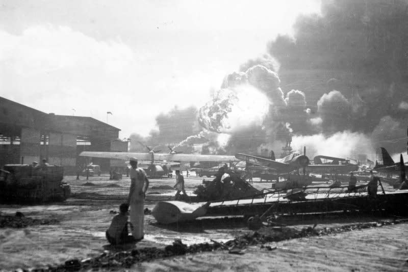 Sailors stand amid wrecked planes at the Ford Island seaplane base, watching as USS Shaw explodes in the center background December 7 1941. USS Nevada is also visible in the middle background, with her bow headed toward the left. File Photo by U.S. Navy/UPI