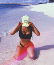 <p>She kneels down in the water posing in a black bikini covering her face with a Calabasas cap.</p>