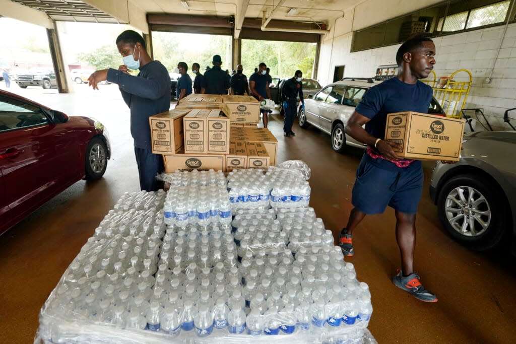 Firefighters and recruits for the Jackson, Miss., Fire Department carry cases of bottled water to residents vehicles, Aug. 18, 2022, as part of the city’s response to longstanding water system problems. (AP Photo/Rogelio V. Solis)