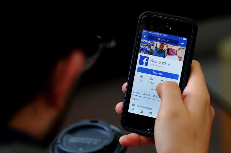 A man pictured from behind holding a phone with the Facebook app open