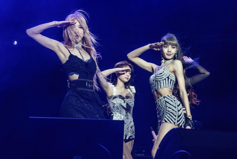 Three women and a fourth semi-obscured saluting on a stage