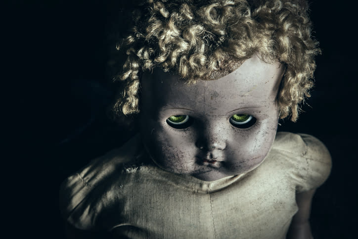 A close-up of an old, worn-out doll with curly hair and eerie eyes, creating a creepy and unsettling atmosphere