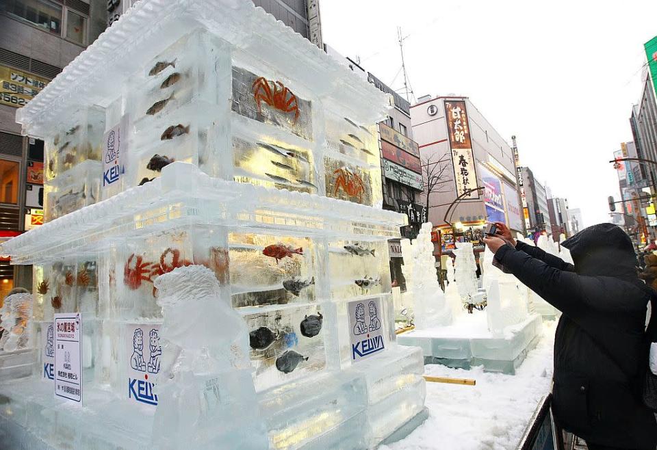 A man takes a photo of an ice sculpture with real fish frozen inside during the 60th Sapporo Snow Festival in Sapporo, Japan.