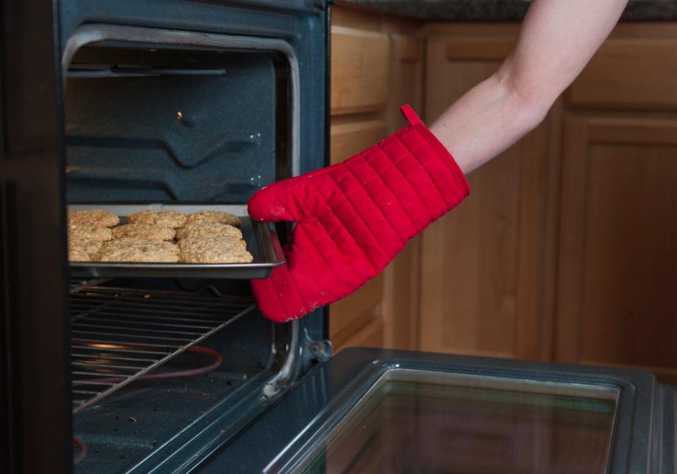 Woman's hand wearing red oven mitt pulling cookies out of oven