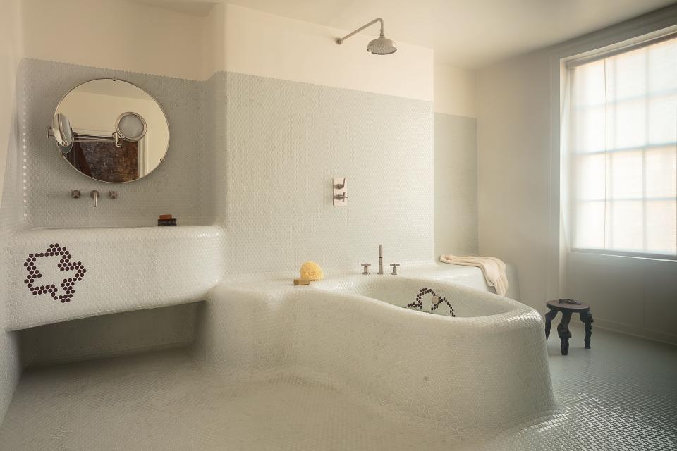 The tiled primary bath features an Eileen Gray mirror from the Invisible Collection and an antique grape-vine stool.