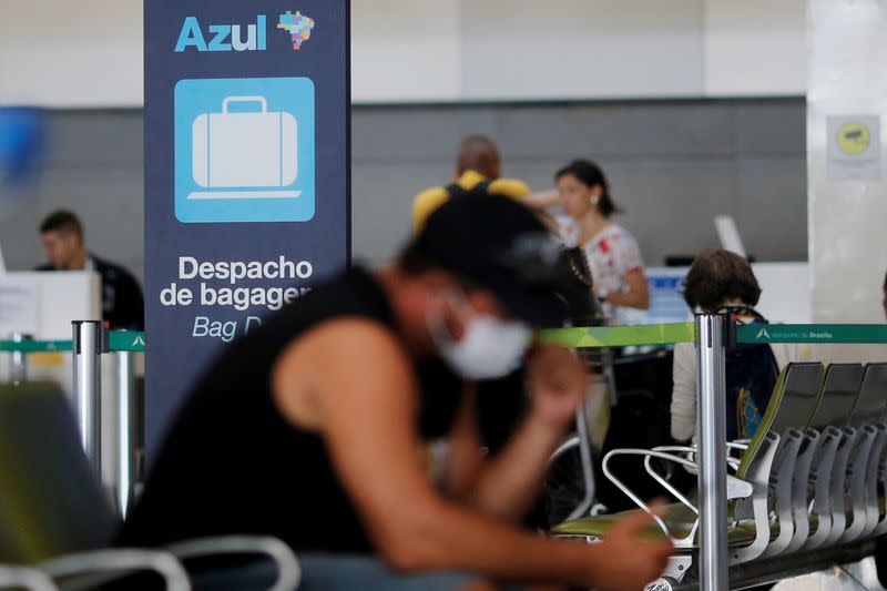 FILE PHOTO: A traveller wearing protective face mask sits in front Azul's air lines check-in at Brazilian International Airport, after reports of the coronavirus in Brasilia