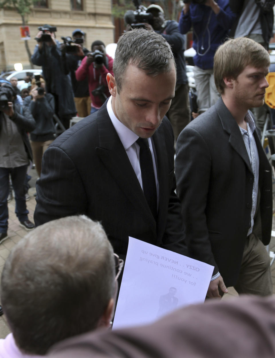 Oscar Pistorius, left, arrives with an unidentified relative as he acknowledges a supporter outside the high court in Pretoria, South Africa, Wednesday, April 16, 2014. Pistorius is charged with murder for the shooting death of his girlfriend Reeva Steenkamp on Valentine's Day in 2013. (AP Photo/Themba Hadebe)