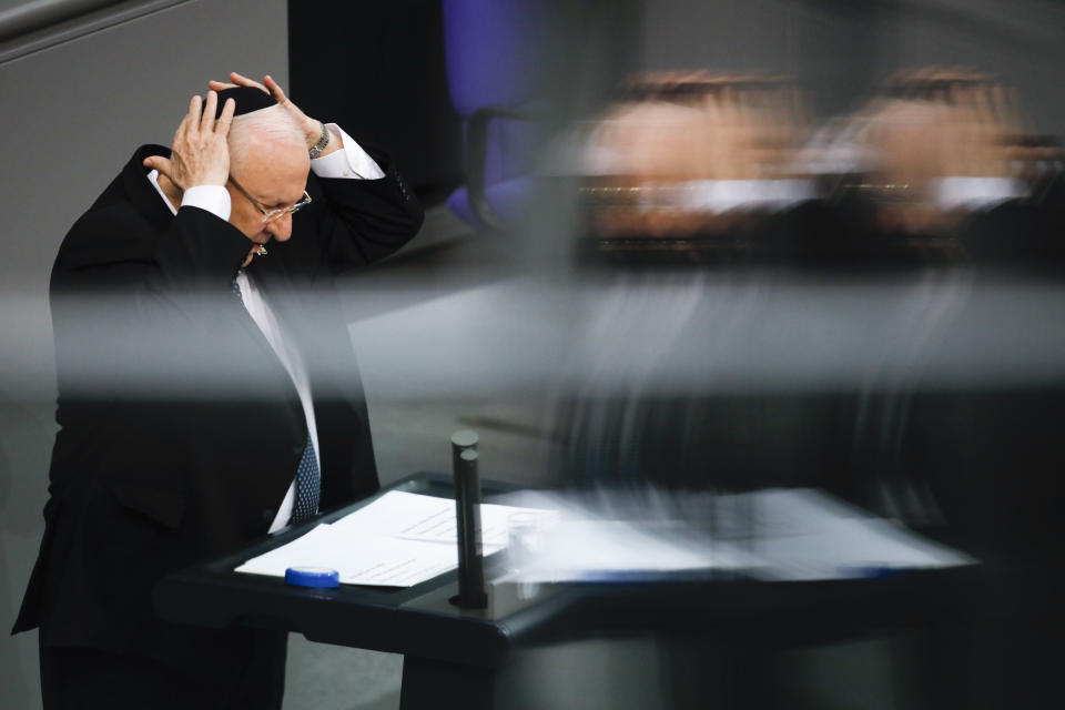 This photo taken with reflections in windows at the visitors tribune, Israel's President Reuven Rivlin takes a kippah on his head as he speeches during a special meeting of the German Parliament Bundestag commemorating the victims of the Holocaust in Berlin, Germany, Wednesday, Jan. 29, 2020. (AP Photo/Markus Schreiber)