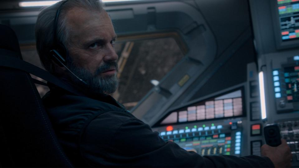 Still from the T.V. show For All Mankind (season 4, episode 1). Close up of a man sitting in the cockpit of a space shuttle. He is around 70 years old with short gray hair and trimmed beard.