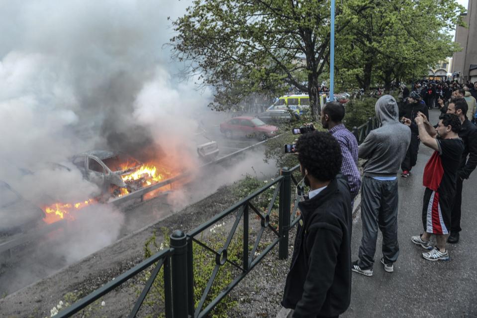 File - Bystanders take photos of a row of burning cars in the Stockholm suburb of Rinkeby after youths rioted in several different suburbs around Stockholm for a fourth consecutive night, in this Thursday May 23, 2013 file photo. Youths in immigrant-heavy Stockholm suburbs torched cars and threw rocks at police in riots believed to be linked to a deadly police shooting of a local resident in the suburb of Husby. There are still plenty of fair-haired people on the streets of Stockholm, but immigration from the Middle East, Africa, Latin America and Asiais rapidly changing the makeup of the nation. (AP Photo/Scanpix, Fredrik Sandberg, file) SWEDEN OUT