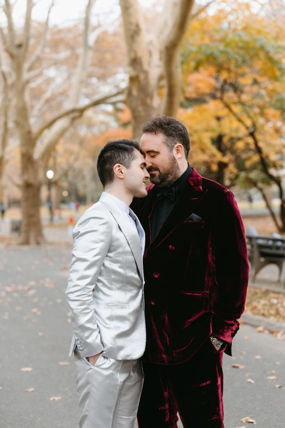 Two grooms lean their heads together in a park.