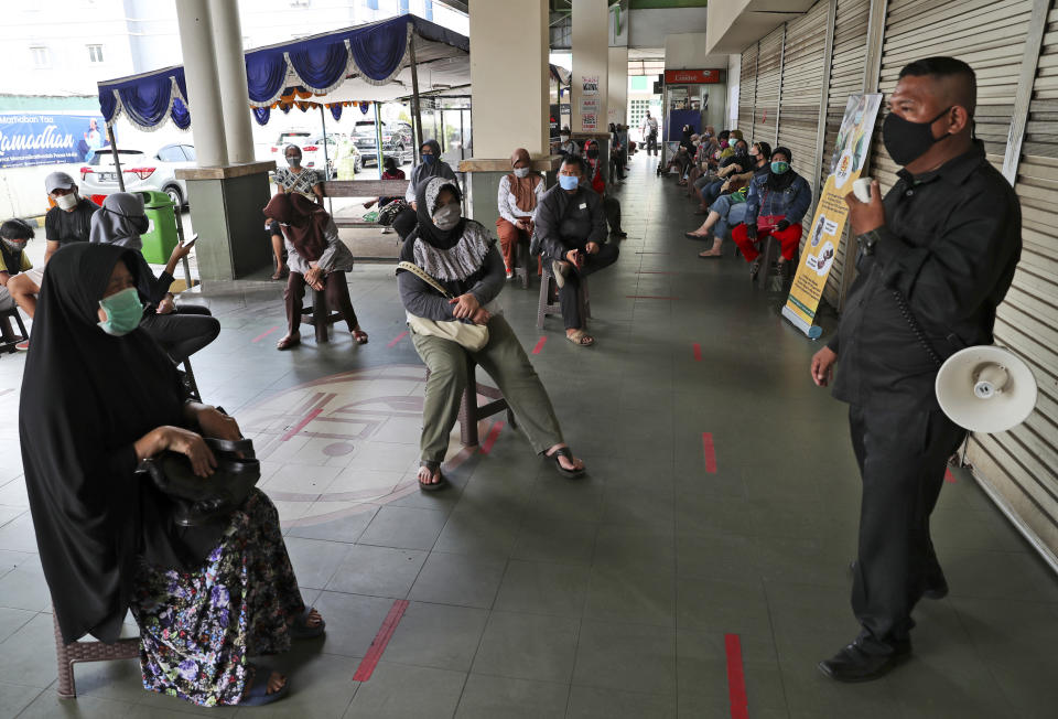 In this April 17, 2020, photo, a security guard speaks through a megaphone as people wearing a face mask sit spaced apart as they practice social distancing to help prevent the spread of the new coronavirus outbreak at a supermarket in Jakarta, Indonesia. While its neighbors scrambled early this year to try to contain the spread of the new coronavirus, the government of the world’s fourth most populous nation insisted that everything was fine. Only after the first cases were confirmed in March did President Joko Widodo acknowledge that his government was deliberately holding back information about the spread of the virus to prevent the public from panicking. The country now has the the highest death toll in Asia after China. (AP Photo/Achmad Ibrahim)