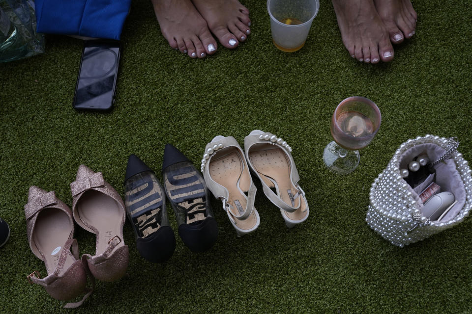 Racegoers take off their shoes to rest their feet on the third day of the Royal Ascot horserace meeting, at Ascot Racecourse, in Ascot, England, Thursday, June 16, 2022. The third day is traditionally known as Ladies Day. (AP Photo/Alastair Grant)