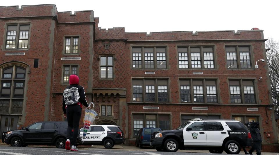 A girl crosses the street near police vehicles outside of Teaneck High School, where at least 60 students were arrested during an overnight break-in, Thursday, May 1, 2014, in Teaneck, N.J. Officers responded to a burglar alarm at the school around 2:30 a.m. Thursday, found urine in the hallways, petroleum jelly on doorknobs, desks flipped over and balloons throughout the building. (AP Photo/Julio Cortez)