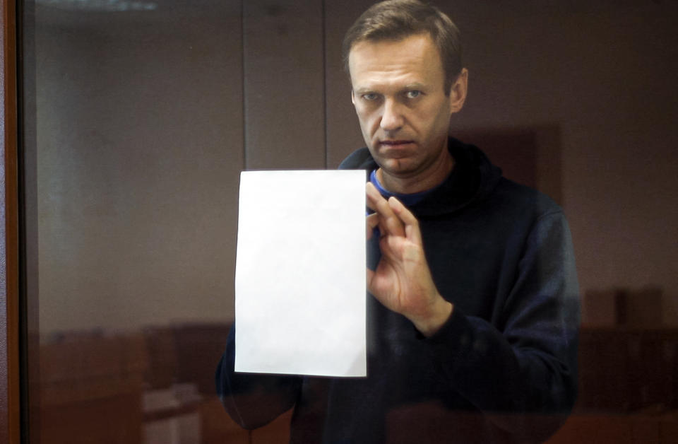 In this photo taken from a footage provided by the Babuskinsky District Court Tuesday, Feb. 16, 2021, Russian opposition leader Alexei Navalny writes notes as he stands in a cage during a hearing on his charges for defamation in the Babuskinsky District Court in Moscow, Russia. Navalny is accused of defaming a World War II veteran who was featured in a video last year advertising constitutional amendments that allowed an extension of President Vladimir Putin's rule. (Babuskinsky District Court Press Service via AP)