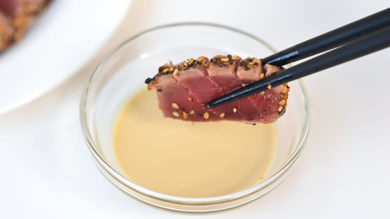 Slice of seared tuna being dipped into sauce