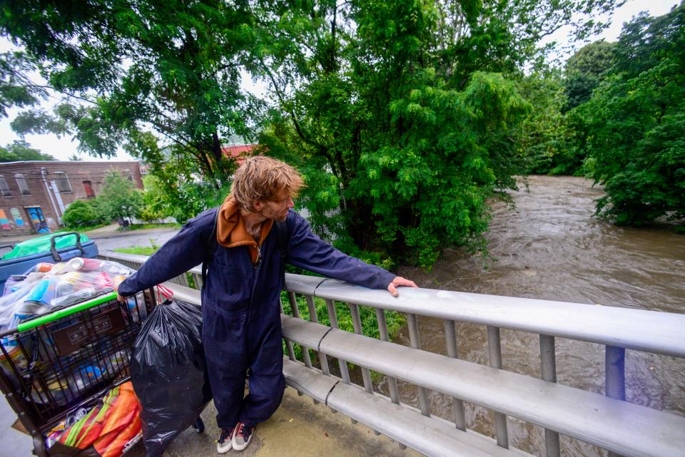 Standing on the Elm Street Bridge with some of his things packed, Jeremiah Ferland, a person facing homelessness in Brattleboro, Vt., looks at the spot where he and others would camp as the water levels of Whetstone Brook rise, Monday, July 10, 2023. (Kristopher Radder/The Brattleboro Reformer via AP)