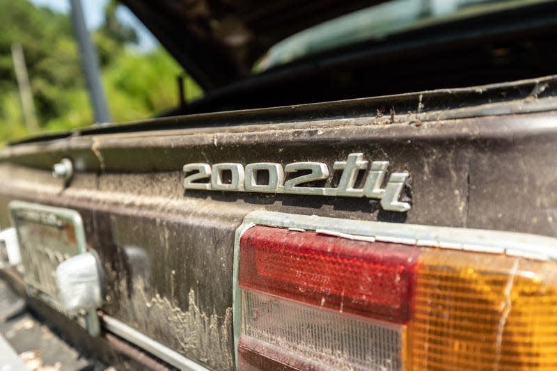 a close-up photo of the 2002tii badge on the back of a very dirty maroon bmw coupe from 1974