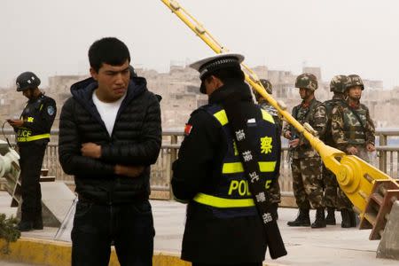 FILE PHOTO: A police officer checks the identity card of a man as security forces keep watch in a street in Kashgar, Xinjiang Uighur Autonomous Region, China, March 24, 2017. REUTERS/Thomas Peter/File Photo