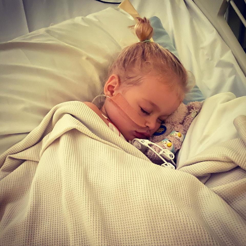 The two-year-old girl is seen here lying in her hospital bed with a tube coming from her nose.