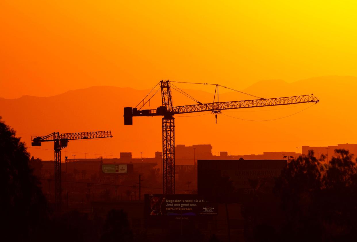 Construction cranes are silhouetted against the colorful sunset in Phoenix on July 13, 2023, the 14th day in a row of temperatures 110 degrees or more.