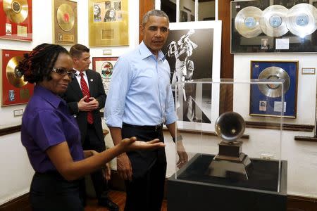 U.S. President Barack Obama looks at a Grammy Award as he gets a tour of the Bob Marley Museum from staff member Natasha Clark (L) in Kingston, Jamaica April 8, 2015. REUTERS/Jonathan Ernst