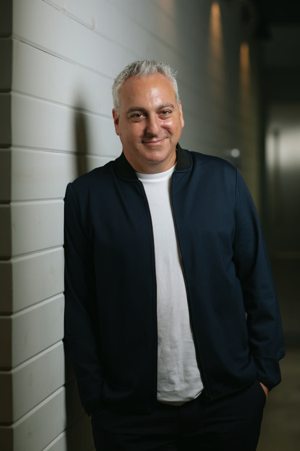 A man leans on a wall and smiles for the camera.