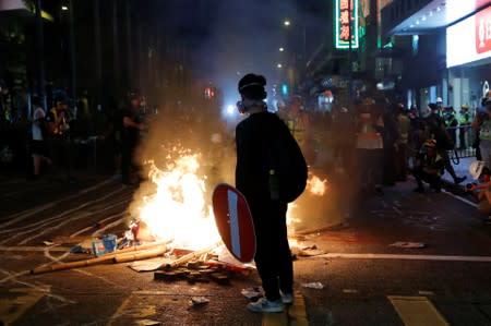 An anti-government protester stands behind a burning barrier during a demonstration, in Hong Kong