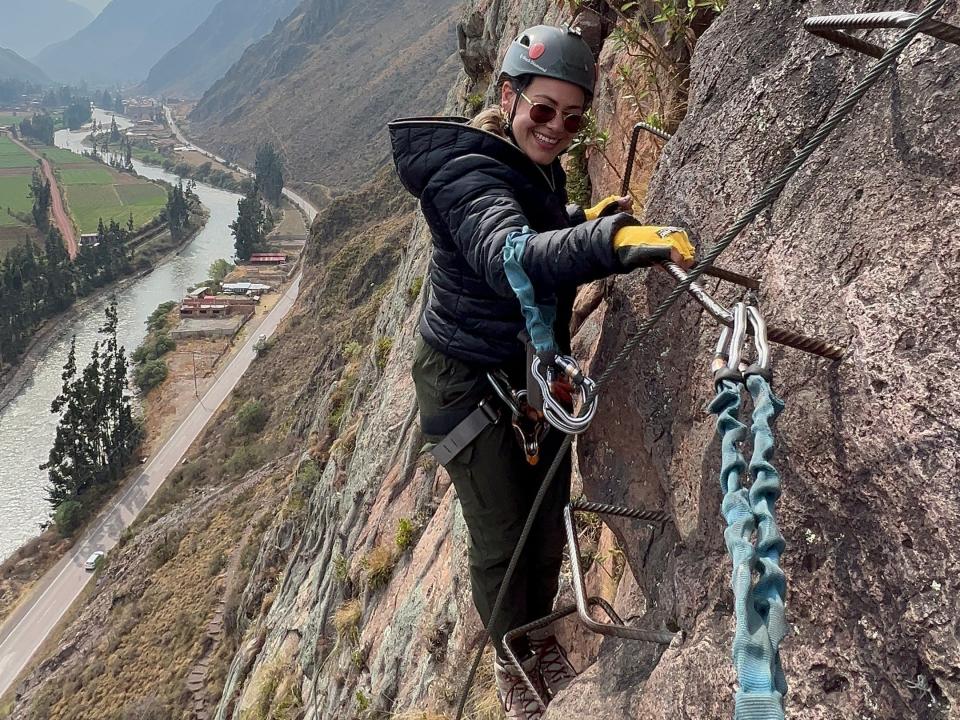 Victoria, wearing a helmet and safety harness, climbs up the mountain via ferrata.