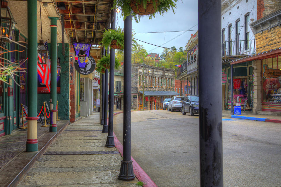 A street in Eureka Springs lined with various shops. One of the signs that says "VooDoo" above a storefront features a skull in a top hat