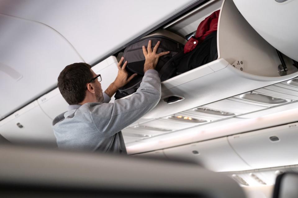 <p>Getty</p> Photo of man trying to fit luggage in overhead bin on airplane.