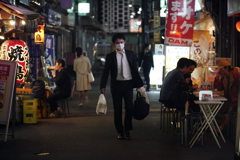 FILE - In this April 28, 2020, file photo, a man wearing a face mask against the spread of the new coronavirus walks through a bar street in Tokyo. Under Japan's coronavirus state of emergency, people have been asked to stay home. Many are not. Some still have to commute to their jobs despite risks of infection, while others are dining out, picnicking in parks and crowding into grocery stores with scant regard for social distancing. (AP Photo/Eugene Hoshiko, File)