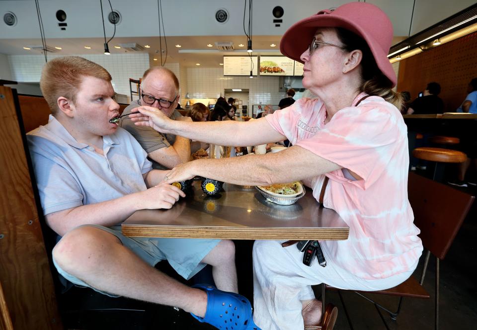 Annette Maughan, right, feeds her son Glenn Maughan, nicknamed Bug, as her husband Glenn Maughan watches, at Chipotle Mexican Grill, in Westminster, Md., on Saturday, July 8, 2023. Bug, age 20, is nonverbal and currently experiences one to three seizures a day. | Kristin Murphy, Deseret News