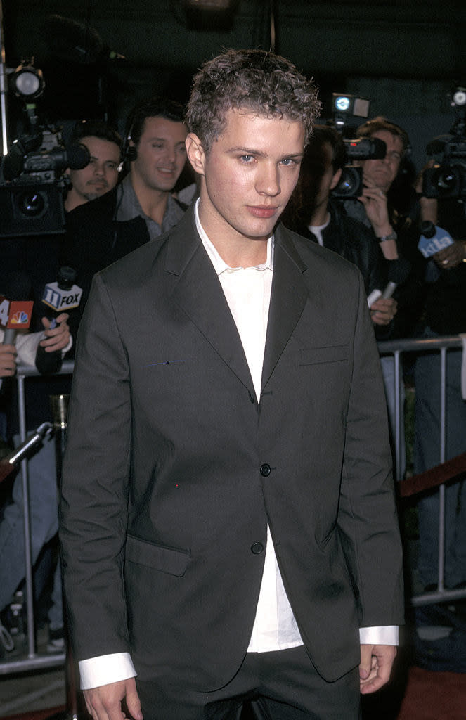 Wearing a suit, no tie, and looking at the camera with paparazzi behind him