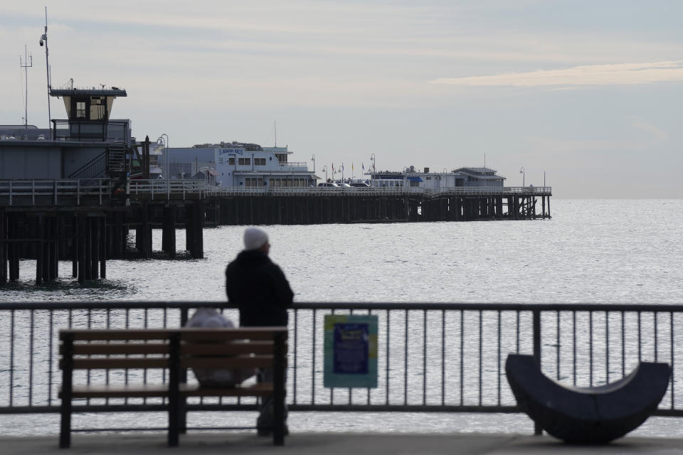 A man looks toward the Santa Cruz Wharf in Santa Cruz, Calif., Friday, Jan. 12, 2024. Rising seas, frequent storms take toll on California's iconic piers, threatening beach landmarks. (AP Photo/Jeff Chiu)