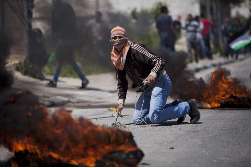 A masked Palestinian takes cover during a protest calling for the release of Palestinian prisoners held in Israeli jails, outside Ofer, an Israeli military prison near the West Bank city of Ramallah, Friday, April 4, 2014. (AP Photo/Majdi Mohammed)