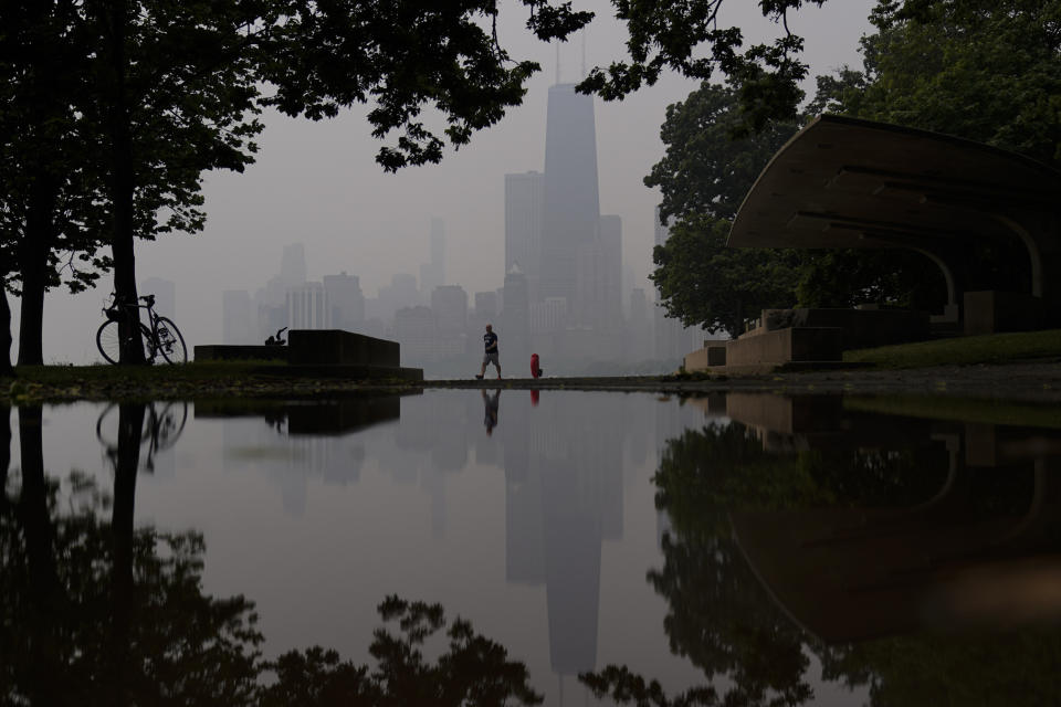 A person walks along the shore of Lake Michigan as the downtown skyline is blanketed in haze from Canadian wildfires Tuesday, June 27, 2023, in Chicago. (AP Photo/Kiichiro Sato)